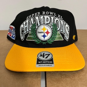 May include: Black and gold adjustable baseball cap. The cap features the text "SUPER BOWL XL CHAMPIONS" in white, with the Steelers logo in the centre. The brim is gold, and the cap has a "47 Hitch" adjustable tag.