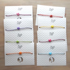 May include: Eight colorful friendship bracelets with Mickey Mouse charms on white cards with a polka dot pattern. The bracelets are made of string and have different colored beads.