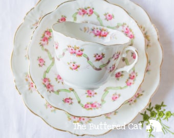 Un antiguo trío de té de porcelana inglesa de Collingwoods, cintas verdes decoradas a mano y rosas rosadas.