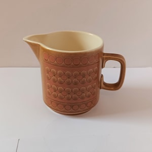 May include: A brown ceramic pitcher with a cream-colored interior and a floral pattern in shades of brown and orange.