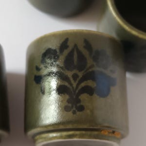 Puede incluir: Una taza de cerámica verde con un diseño floral negro y azul. La taza tiene un borde dorado.