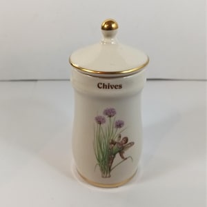 May include: A cream-coloured ceramic chives jar with a lid and gold trim. The jar features a painted illustration of purple chive flowers and a fairy. The word "Chives" is printed on the front.