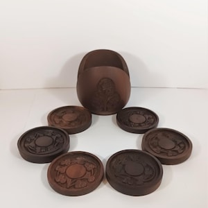 May include: A set of seven dark brown wooden coasters with a matching holder. Each coaster and the holder feature carved floral designs. The coasters are round and the holder is oval-shaped.