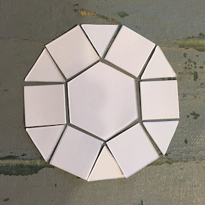 May include: A white paper geometric shape made of 12 pieces. The shape is a dodecagon, a 12-sided polygon. The pieces are arranged in a symmetrical pattern.