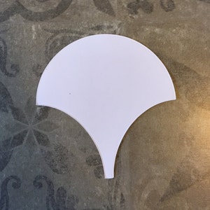 May include: White ceramic tile in the shape of a fan with a pointed bottom.