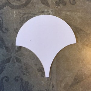 May include: White ceramic tile in the shape of a scallop shell.