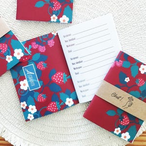 Peut inclure: Trois petits carnets rouges avec un motif de fraises et de feuilles. Les carnets ont un bandeau en papier brun avec le texte "Chut!" dessus. Les carnets sont sur une surface blanche.