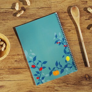 K&ouml;nnte beinhalten: Ein blaues Spiralnotizbuch mit einem floralen Design mit roten Beeren, gelben Zitronen und einem orangefarbenen K&uuml;rbis. Das Notizbuch hat eine wei&szlig;e Spiralbindung.