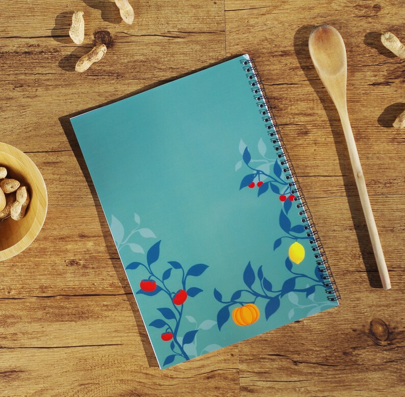 K&ouml;nnte beinhalten: Ein blaues Spiralnotizbuch mit einem floralen Design mit roten Beeren, gelben Zitronen und einem orangefarbenen K&uuml;rbis. Das Notizbuch hat eine wei&szlig;e Spiralbindung.