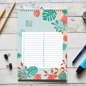 May include: A wall calendar page for the month of May featuring a light blue background with a botanical pattern of coral and dark green leaves. The center contains a white grid with numbered lines from 1 to 31 for daily planning entries.