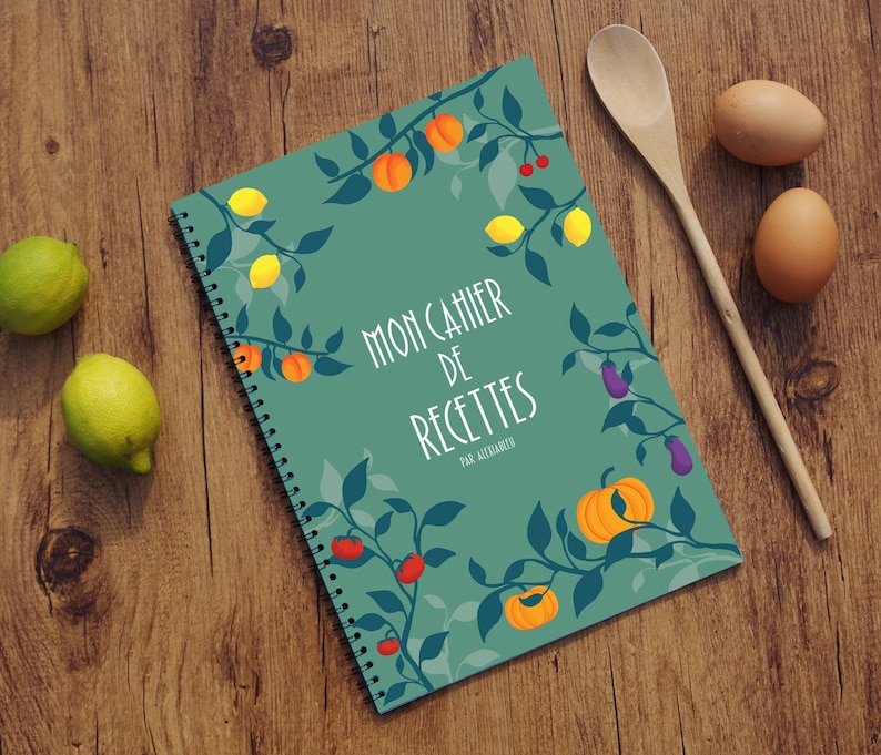 K&ouml;nnte beinhalten: Ein gr&uuml;nes spiralgebundenes Notizbuch mit einem Blattdesign und dem Text "Mon Cahier de Recettes Par Alexandra". Das Notizbuch zeigt Illustrationen von Zitronen, K&uuml;rbissen, Tomaten und Auberginen.
