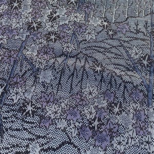 May include: A rectangular textile with a detailed floral and landscape design. The pattern features a combination of purple, white, and black elements, creating a textured appearance. The edges are finished with a black border.
