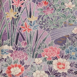 Pode incluir: Close-up de um tecido floral com fundo roxo. O design apresenta várias flores em tons de rosa, vermelho, branco e azul, juntamente com folhagens verdes e caules verdes e roxos finos. O padrão é intrincado e detalhado.