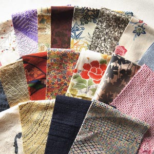 May include: A collection of rectangular fabric swatches arranged in a fan shape, featuring a variety of patterns including floral, geometric, and abstract designs in colors such as red, blue, pink, yellow, black, and white with diverse textures.
