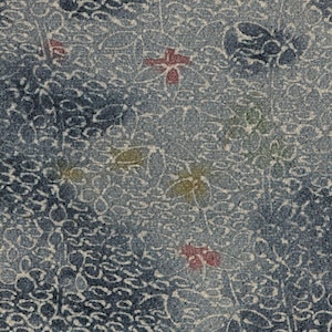 Può includere: Primo piano di un tessuto blu con un motivo floreale. Il design presenta fiori e foglie bianche, rosse e gialle su uno sfondo strutturato. Il tessuto ha un aspetto simile al denim.