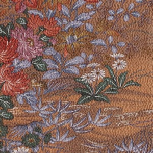 Pode incluir: Close-up de um tecido com um padrão floral. O design apresenta flores vermelhas, rosa e brancas com folhas verdes e folhagem azul-acinzentada sobre um fundo castanho. O tecido tem uma aparência texturizada.