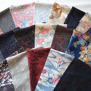 May include: A collection of folded fabric squares, each displaying a unique pattern and color palette. The fabrics feature floral, geometric, and abstract designs in shades of blue, red, pink, and gold. The arrangement suggests a variety of textiles.