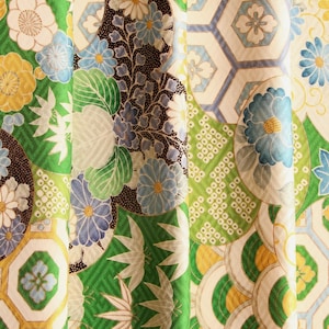 Op de afbeelding: Een stof met een levendig patchworkontwerp in groen, geel, blauw en wit. Het patroon bevat herhalende zeshoekige geometrische vormen, gestileerde bloemmotieven en illustraties van bamboebladeren met een geweven textuur.