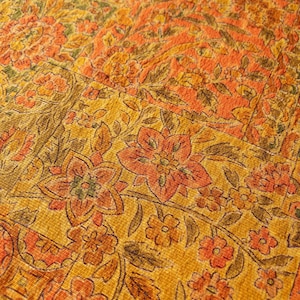 May include: A textile fabric featuring a repeating patchwork pattern of floral motifs in shades of mustard yellow, burnt orange, and dark olive green. The design consists of rectangular sections filled with intricate blossoms and leafy vines.