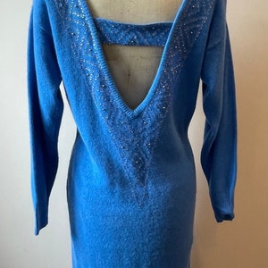 May include: A blue knitted sweater dress with a low back and a beaded design. The dress has long sleeves and a fitted silhouette.