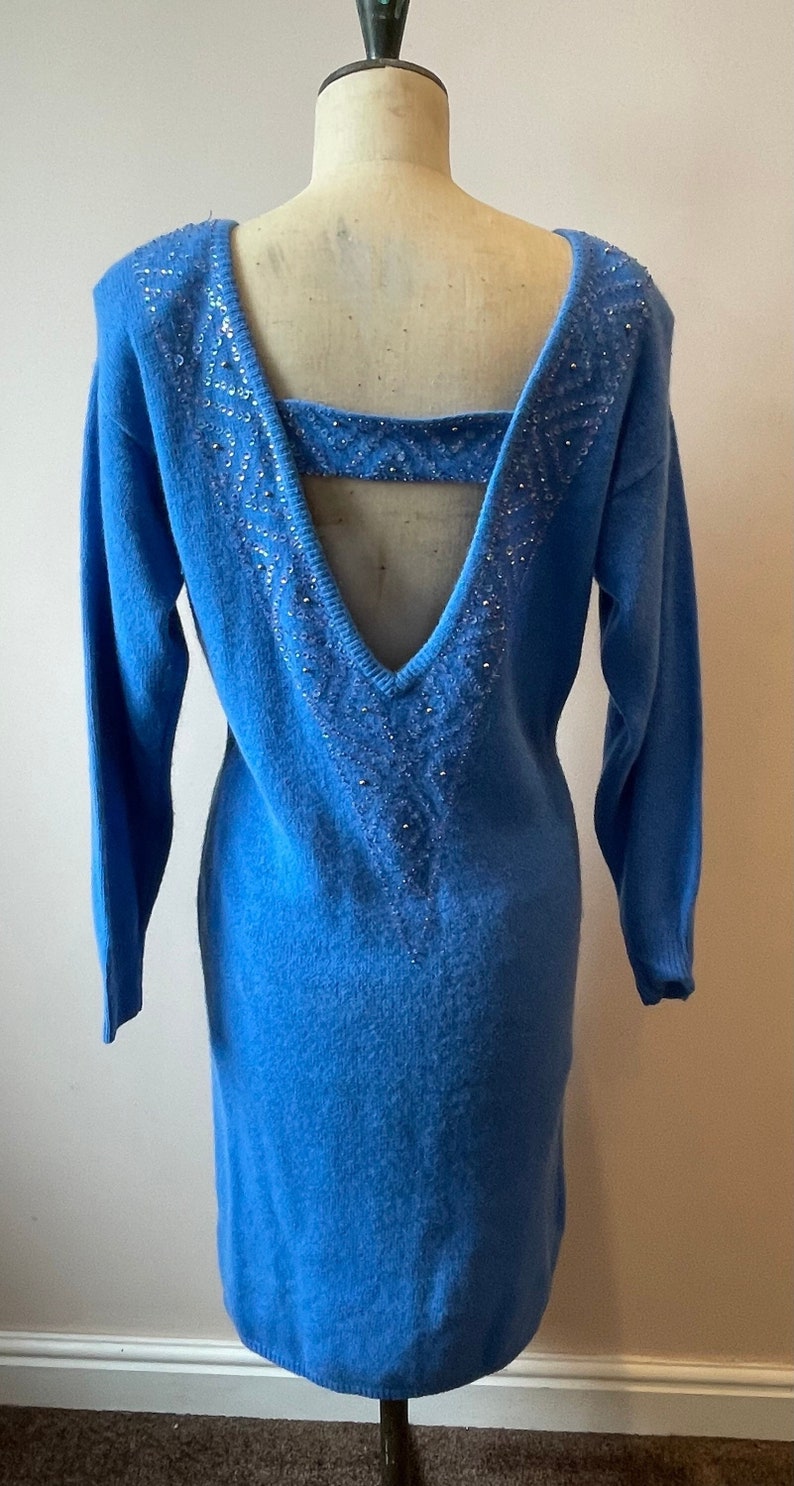 May include: A blue knitted sweater dress with a low back and a beaded design. The dress has long sleeves and a fitted silhouette.