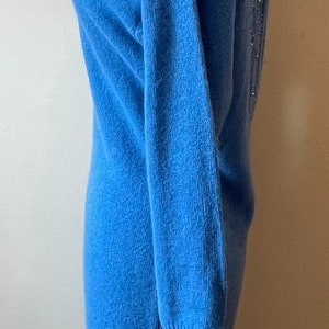 May include: A blue knitted sweater dress with a beaded back detail. The dress is on a mannequin and has long sleeves.