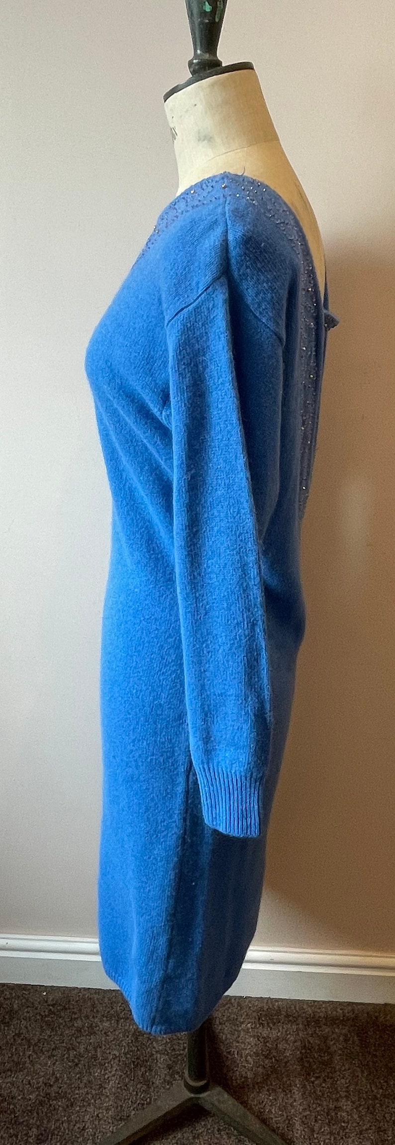 May include: A blue knitted sweater dress with a beaded back detail. The dress is on a mannequin and has long sleeves.