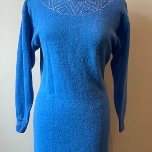 May include: A blue sweater dress with a beaded neckline. The dress is on a mannequin.