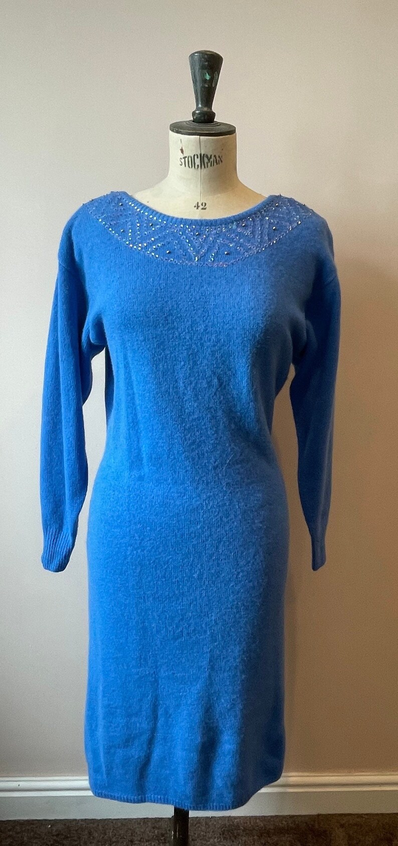 May include: A blue sweater dress with a beaded neckline. The dress is on a mannequin.