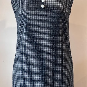 May include: Sleeveless navy blue dress with a white lace collar and three white buttons. The dress has a textured, grid-like pattern. The dress is displayed on a mannequin.