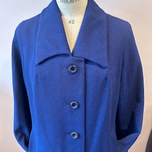 May include: A vintage cobalt blue coat with a textured weave. The coat features a wide collar, three matching buttons, and a tailored fit. The coat is displayed on a mannequin with the word "STOCKMAN" and the number "42" visible.