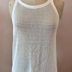 May include: A white, open-weave tank top on a mannequin. The top has a round neckline and a loose, breathable design. The mannequin is a vintage style with the word "STOCKMAN" printed on the top.