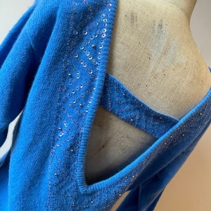 May include: A blue knitted sweater with a low back and sequined detailing. The sequins are arranged in a geometric pattern.