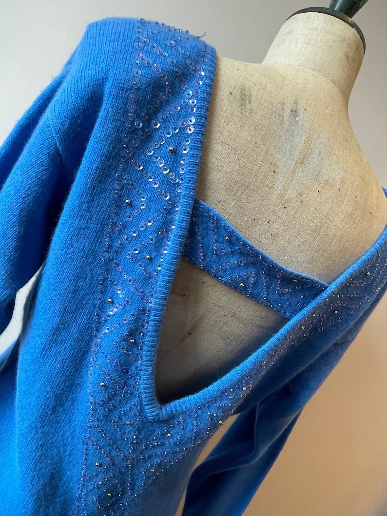 May include: A blue knitted sweater with a low back and sequined detailing. The sequins are arranged in a geometric pattern.