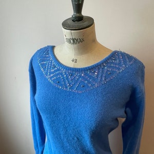 May include: A light blue sweater with a sequined neckline. The sequins are iridescent and create a geometric pattern.