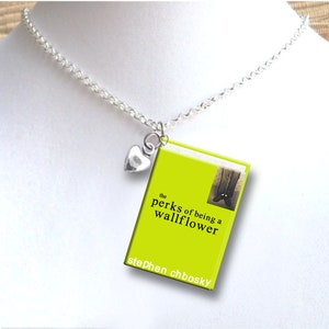 May include: A silver-toned necklace featuring a small heart charm and a book pendant. The book pendant has a bright green cover with the title "the perks of being a wallflower" and the author's name, Stephen Chbosky.