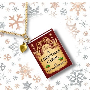 May include: Gold-toned necklace with a small heart charm and a pendant shaped like a book. The book pendant is burgundy with gold lettering and the title "A Christmas Carol" by Charles Dickens.