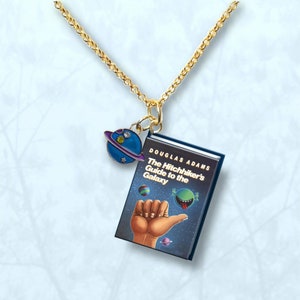 May include: A gold chain necklace with a charm of a book titled "The Hitchhiker's Guide to the Galaxy" by Douglas Adams. The charm also features a small blue planet with a purple ring.