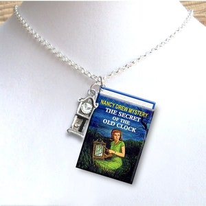 May include: A silver chain necklace with a charm of a vintage clock and a miniature book cover. The book cover is blue with a picture of a woman sitting by a clock and the text "NANCY DREW MYSTERY THE SECRET OF THE OLD CLOCK".