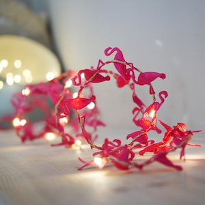 May include: Pink flamingo string lights with warm white LED bulbs. The lights are strung together in a circle and are perfect for adding a festive touch to any room.