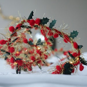 Puede incluir: Una cadena de luces con bayas rojas, purpurina dorada y hojas de acebo verdes. Las luces están conectadas con un cable transparente y son perfectas para añadir un toque festivo a cualquier habitación.