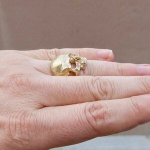 May include: A gold-colored skull ring worn on a person's finger.