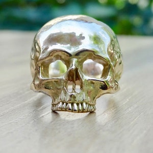 May include: A silver skull ring with a detailed design. The ring is made of metal and has a smooth, polished finish.