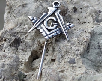 May include: Silver Masonic pin with a square and compass design. The pin has a long, thin stem.
