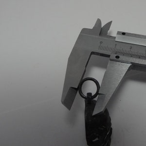 May include: A silver metal caliper measuring the diameter of a silver metal ring attached to a black metal chain.