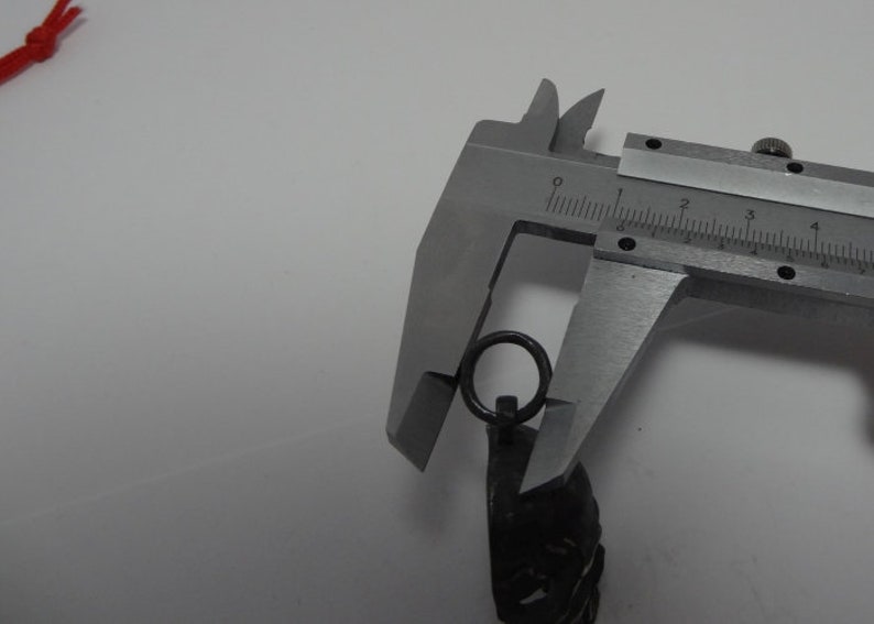 May include: A silver metal caliper measuring the diameter of a silver metal ring attached to a black metal chain.