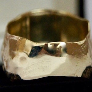 May include: A gold ring with a hammered, textured finish. The ring is wide and has a rounded shape.