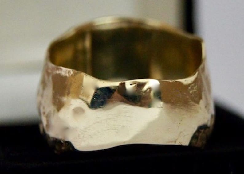May include: A gold ring with a hammered, textured finish. The ring is wide and has a rounded shape.
