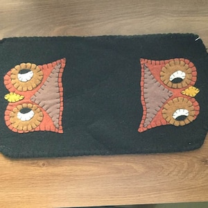 May include: A black felt table runner with two brown and orange owl appliques. The owls have white eyes and yellow beaks.