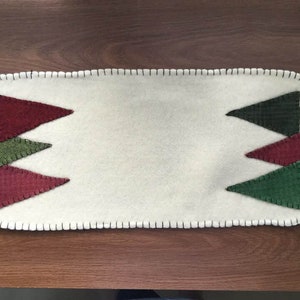 May include: White felt table runner with a stitched border and green and red felt Christmas tree appliques.